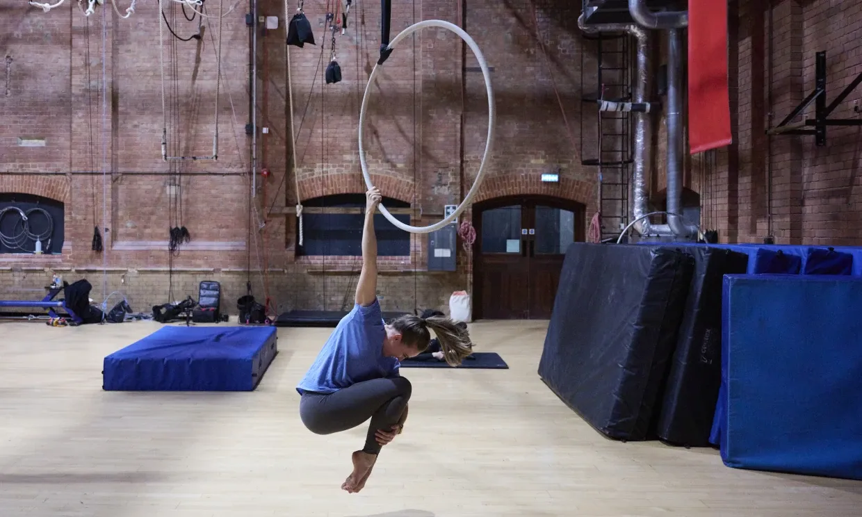 A woman hangs from an aerial hoop by one arm.