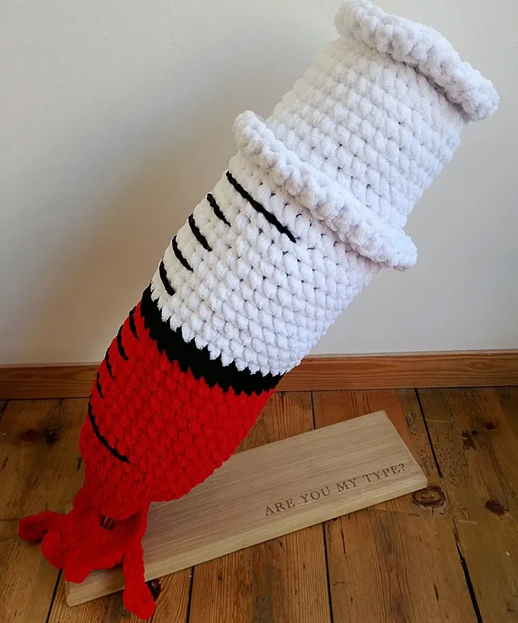 A large knitted syringe with blood leaking out of the needle point.